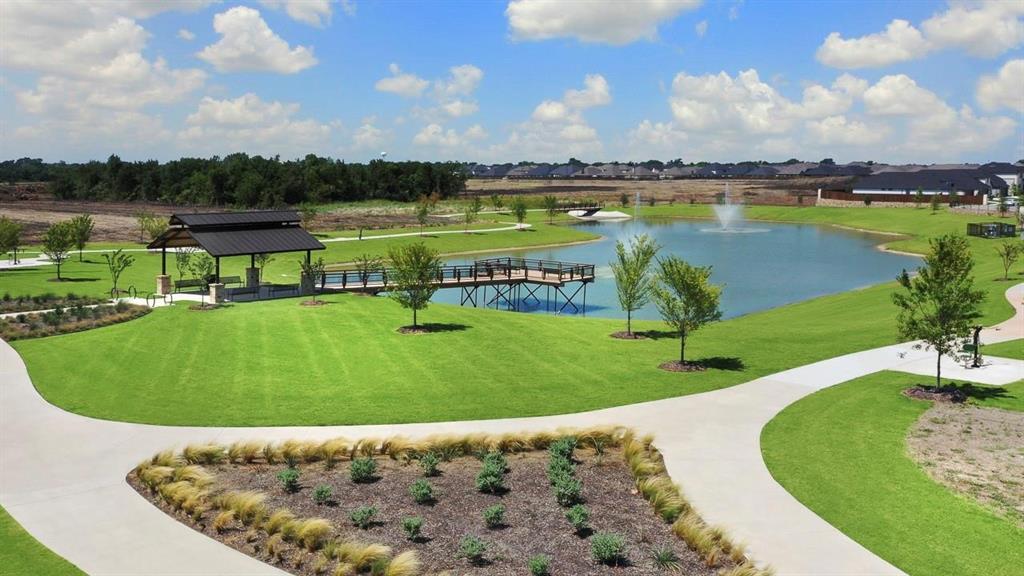 Expansive community grounds featuring a central pond with a fountain, a metal-roofed pavilion, a wooden dock, and concrete walking paths