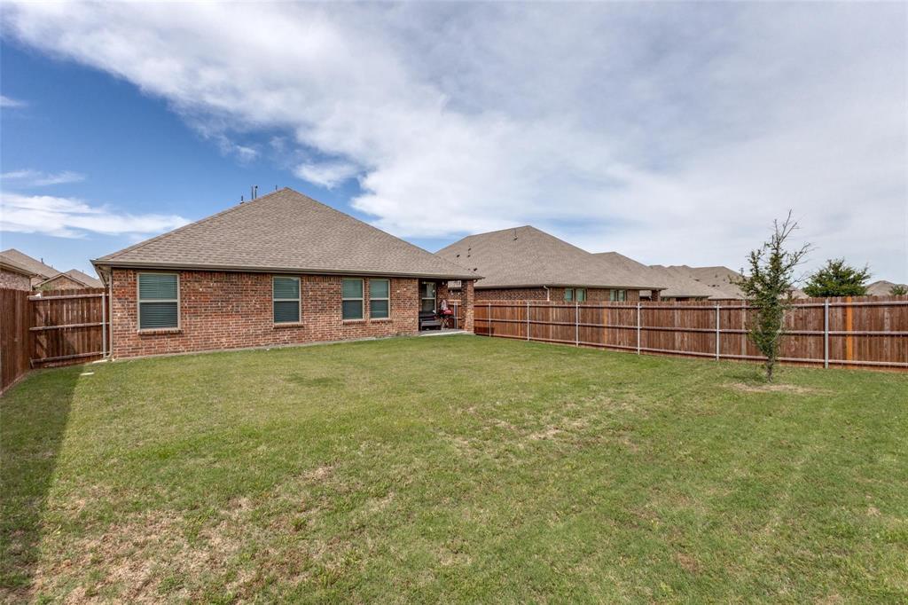 Exterior featuring red brick construction, hip roofline with architectural shingles, and a privacy wood-slat fence enclosing the grass lawn