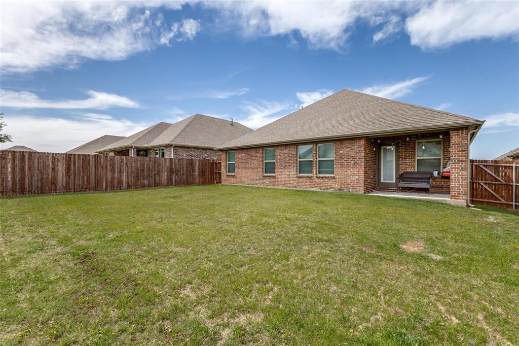 Rear exterior featuring a brick facade, covered concrete patio, and fenced backyard with grass lawn