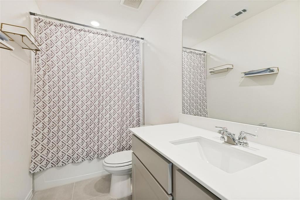 Bathroom featuring a vanity with a white solid-surface countertop, an integrated rectangular sink, polished chrome faucet, expansive wall-mounted mirror, and tile flooring
