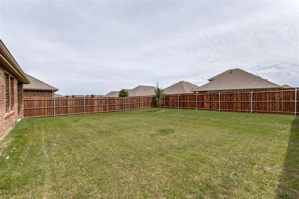 Backyard featuring a grass lawn, perimeter wood fence, and brick home exterior