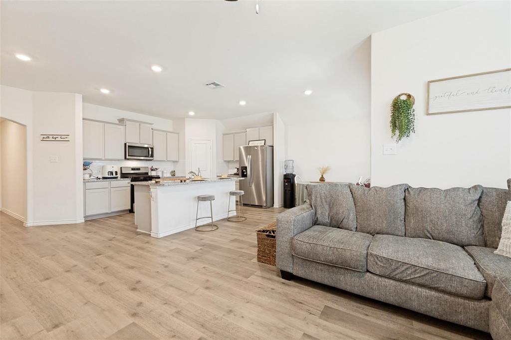 Kitchen featuring light-toned cabinetry, stone-finish countertops, stainless steel appliances, and a center island with bar seating, complemented by wood-finish flooring and recessed lighting