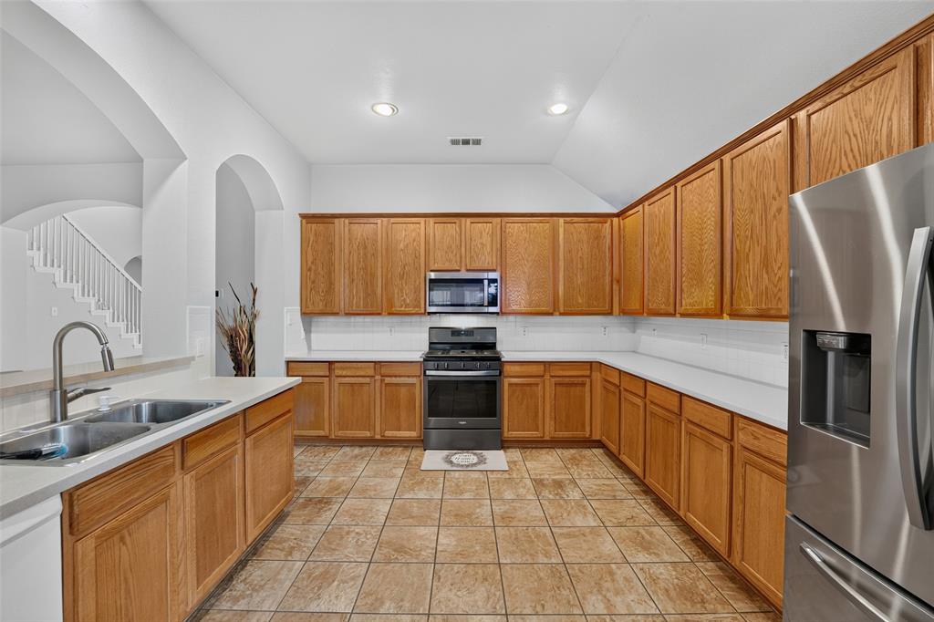Kitchen featuring shaker-style wood cabinetry, stainless steel appliances, ceramic tile flooring, and solid-surface countertops