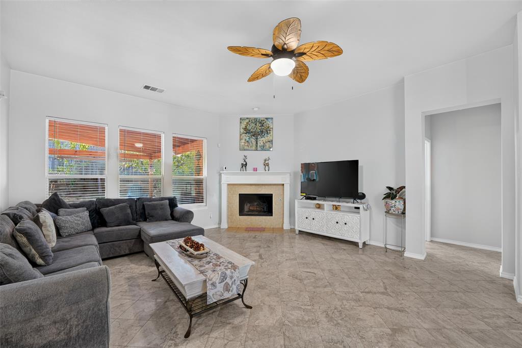 Living area featuring tile flooring, a central fireplace with a decorative surround, and a ceiling fan with leaf-patterned blades