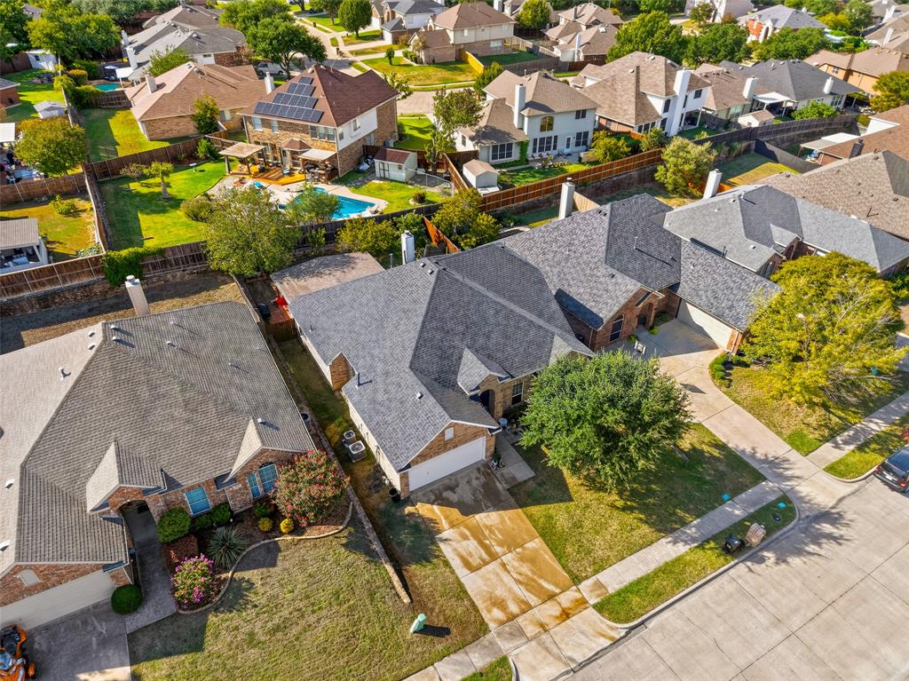 Aerial perspective featuring a multi-hipped asphalt shingle roof, masonry exterior, multi-car garage, concrete driveway, and established landscape