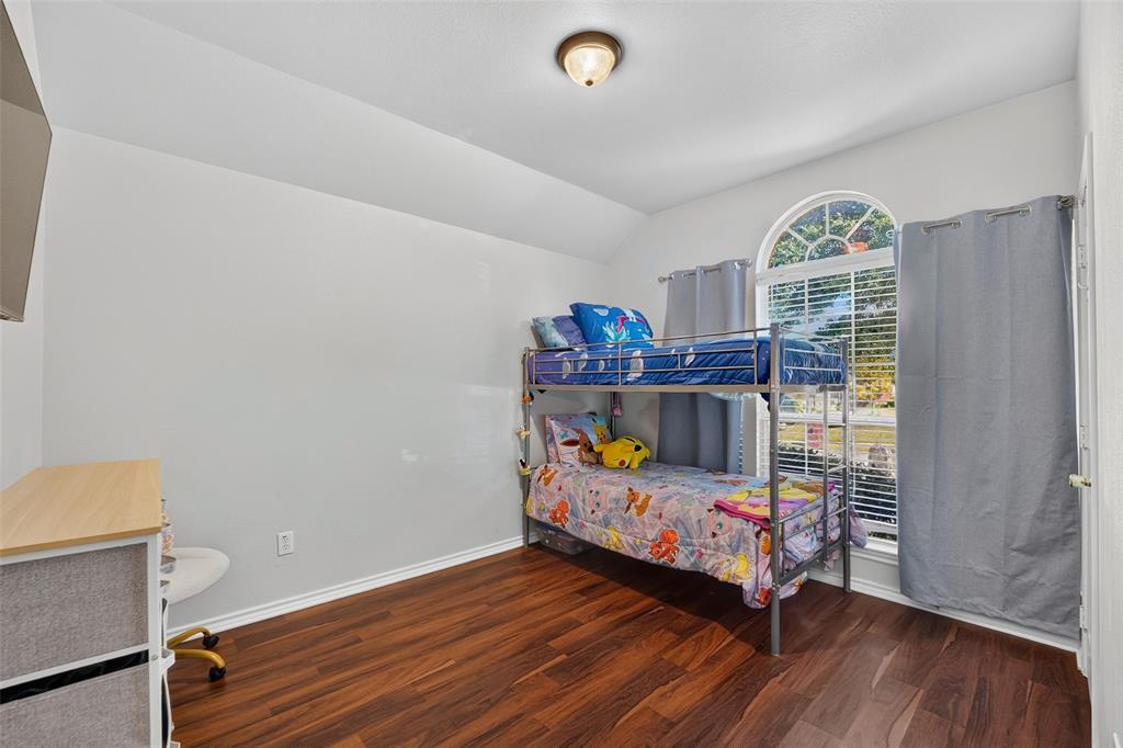 Room featuring vaulted ceilings, wood-finish flooring, and an arched window with integrated muntins, illuminated by a flush-mount ceiling fixture