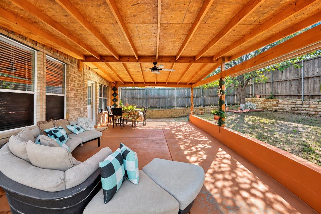 Covered patio featuring an exposed-beam wood ceiling, stamped concrete flooring, a ceiling fan, and a built-in stone retaining wall