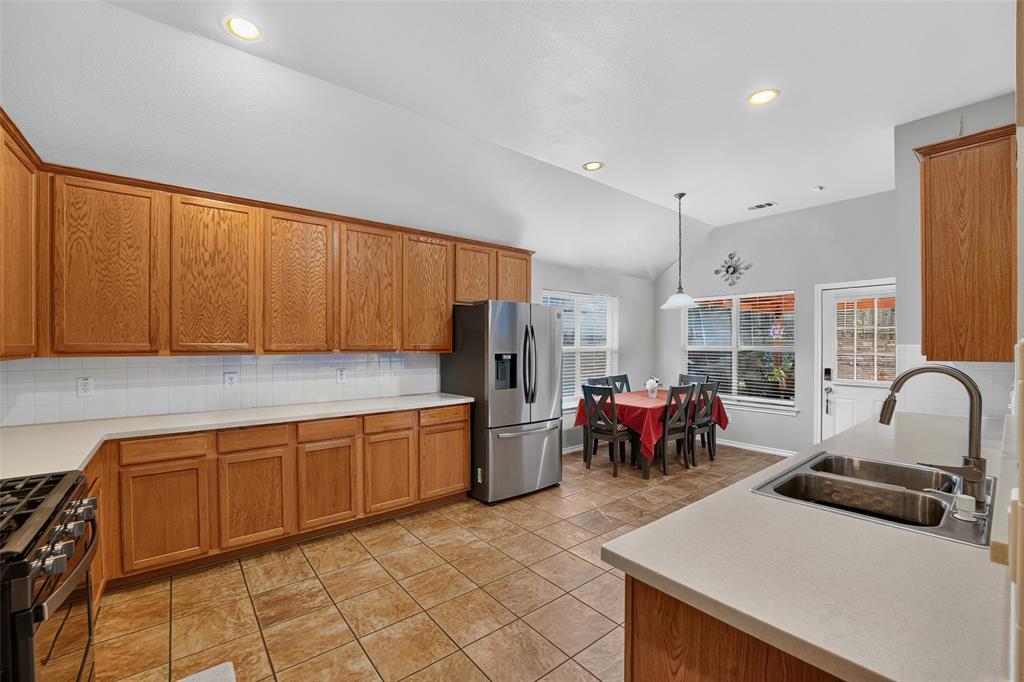 Kitchen featuring wood cabinetry, solid-surface countertops, tile flooring, stainless steel refrigerator, and recessed lighting
