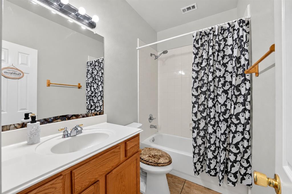Bathroom featuring a vanity with a white solid-surface countertop, an integrated oval basin, and wood-finish cabinetry, paired with a shower-tub combination with tile surround and a multi-light fixture over the mirror