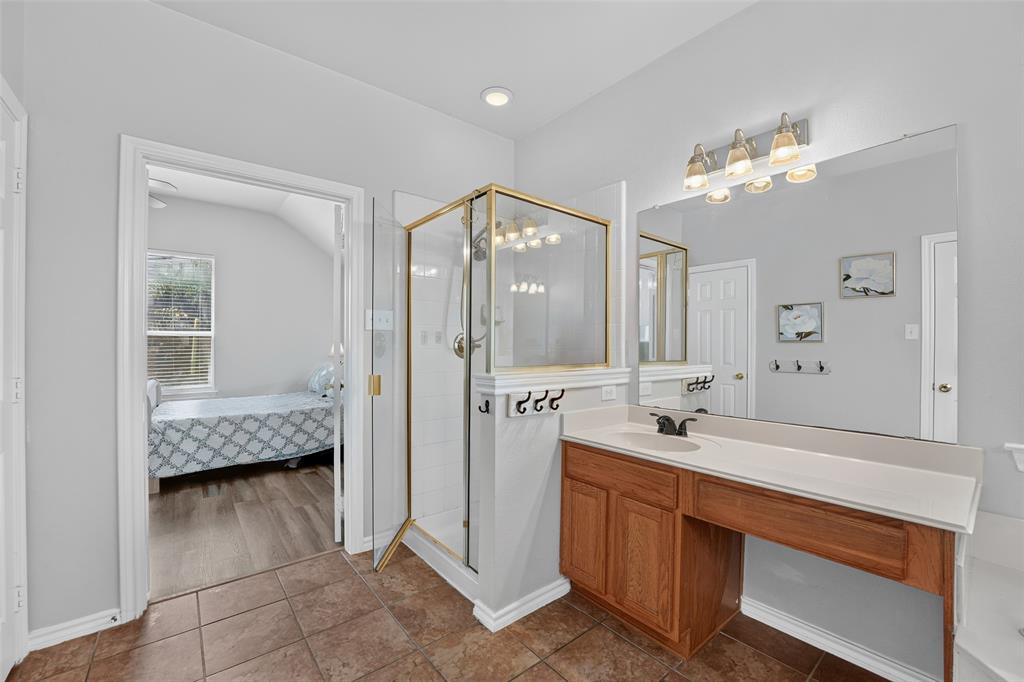 Bathroom featuring a walk-in shower with a gold-tone frame, vanity with an integrated sink, large wall-mounted mirror, and tile flooring