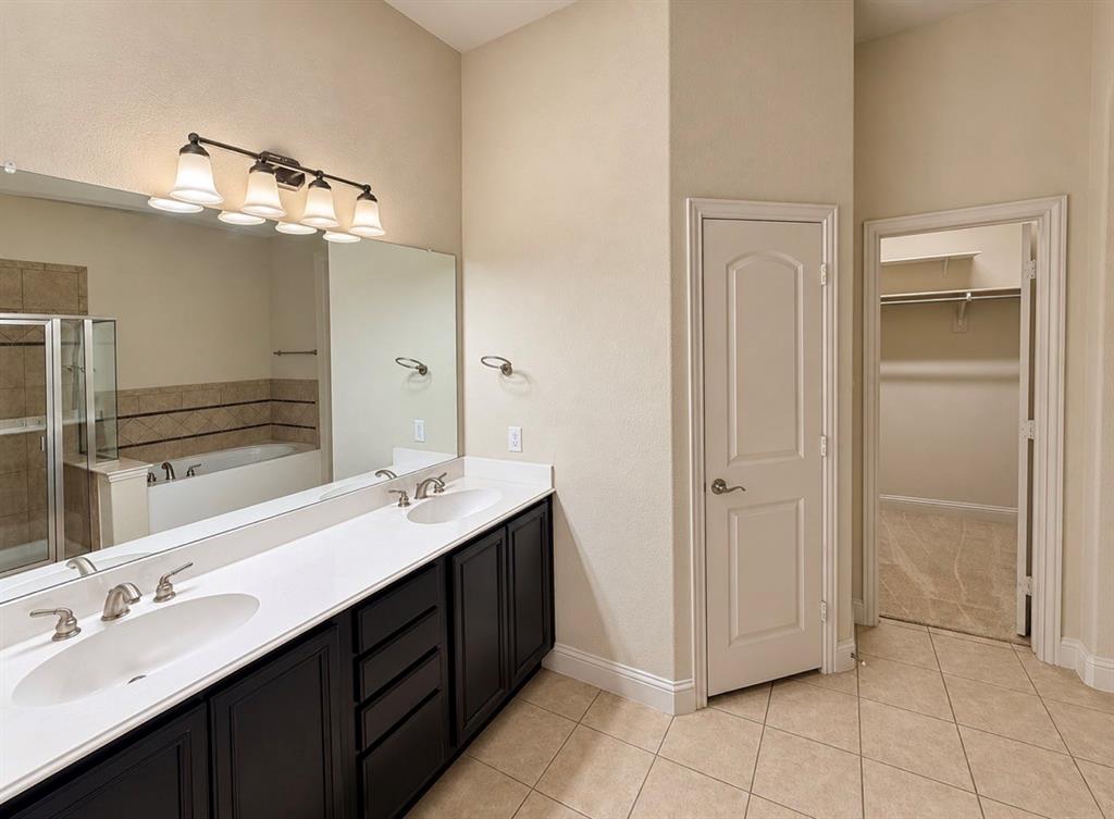 Dual-sink vanity with white countertops and dark-finish cabinetry, full-width wall mirror, four-light vanity fixture, built-in soaking tub, and tile flooring