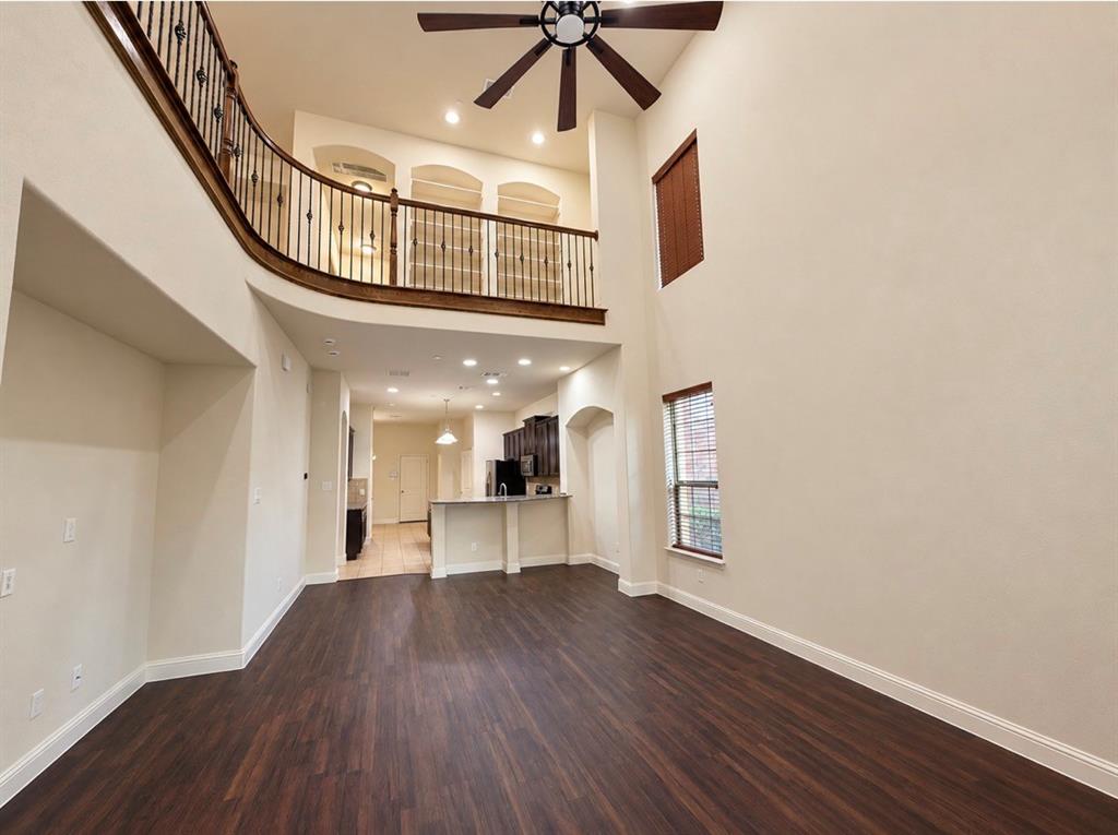 Double-height ceiling featuring a ceiling fan, wood-finish flooring, and an elevated mezzanine with dark metal balusters Double-height ceiling featuring a ceiling fan, wood-finish flooring, and an elevated mezzanine with dark metal balusters