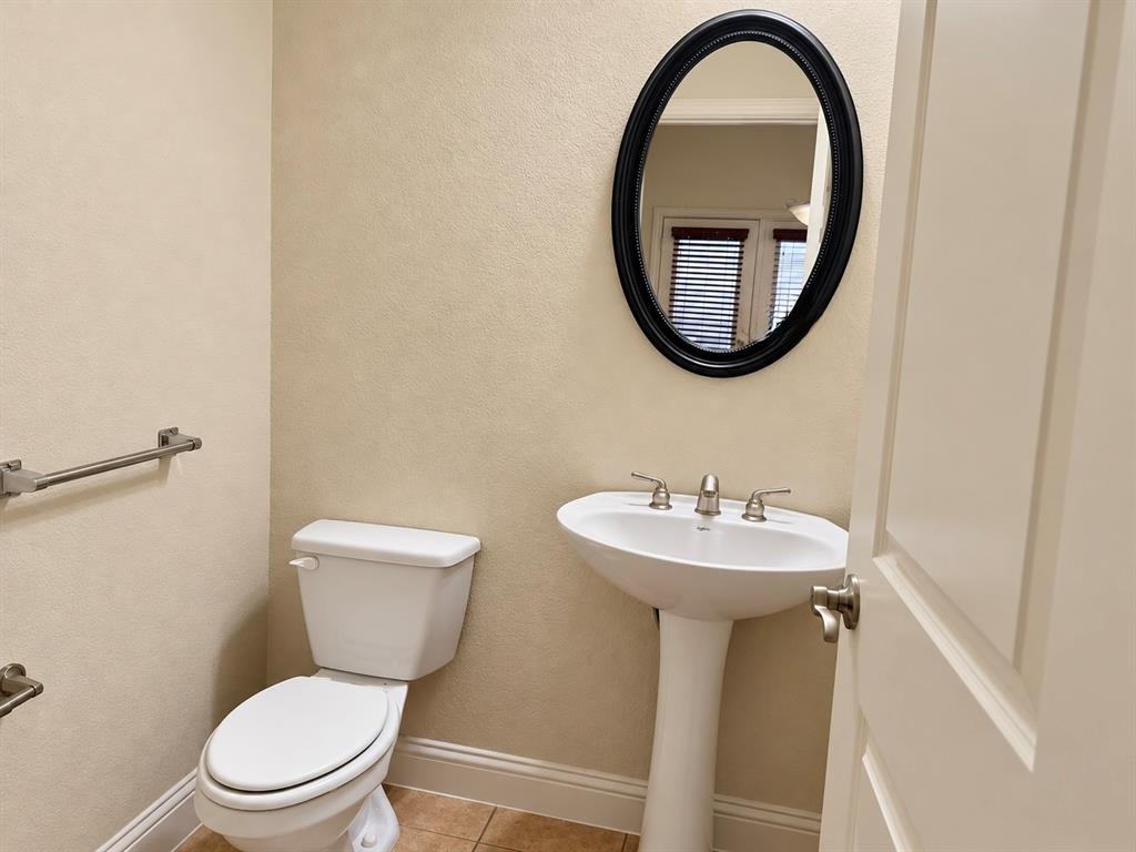 Pedestal sink with a widespread faucet, oval wall mirror with a black frame, ceramic tile flooring, and brushed nickel hardware