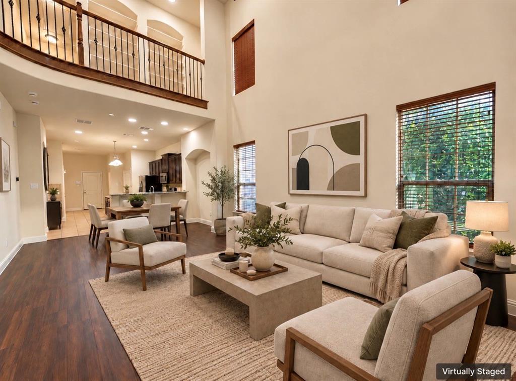 Two-story living area featuring expansive ceilings, wood-finish flooring, recessed lighting, and a metal-railed mezzanine balcony