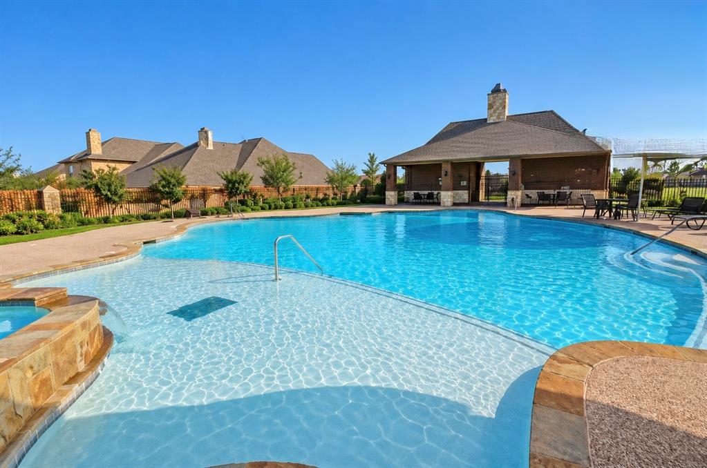Swimming pool with stone-finished edging, integrated spa, and covered pavilion featuring a stone hearth