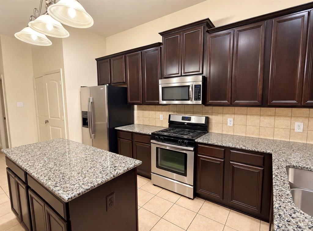 Kitchen featuring dark wood cabinetry, speckled stone-finish countertops, stainless steel appliances, a central island, and tile flooring Kitchen featuring dark wood cabinetry, speckled stone-finish countertops, stainless steel appliances, a central island, and tile flooring