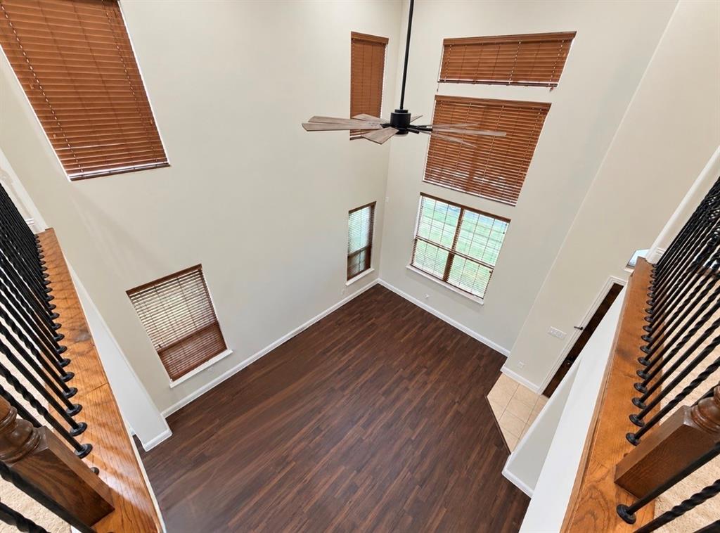 Double-height ceiling, wood-finish flooring, multi-level windows, wrought iron railing with wood accents, and ceiling fan