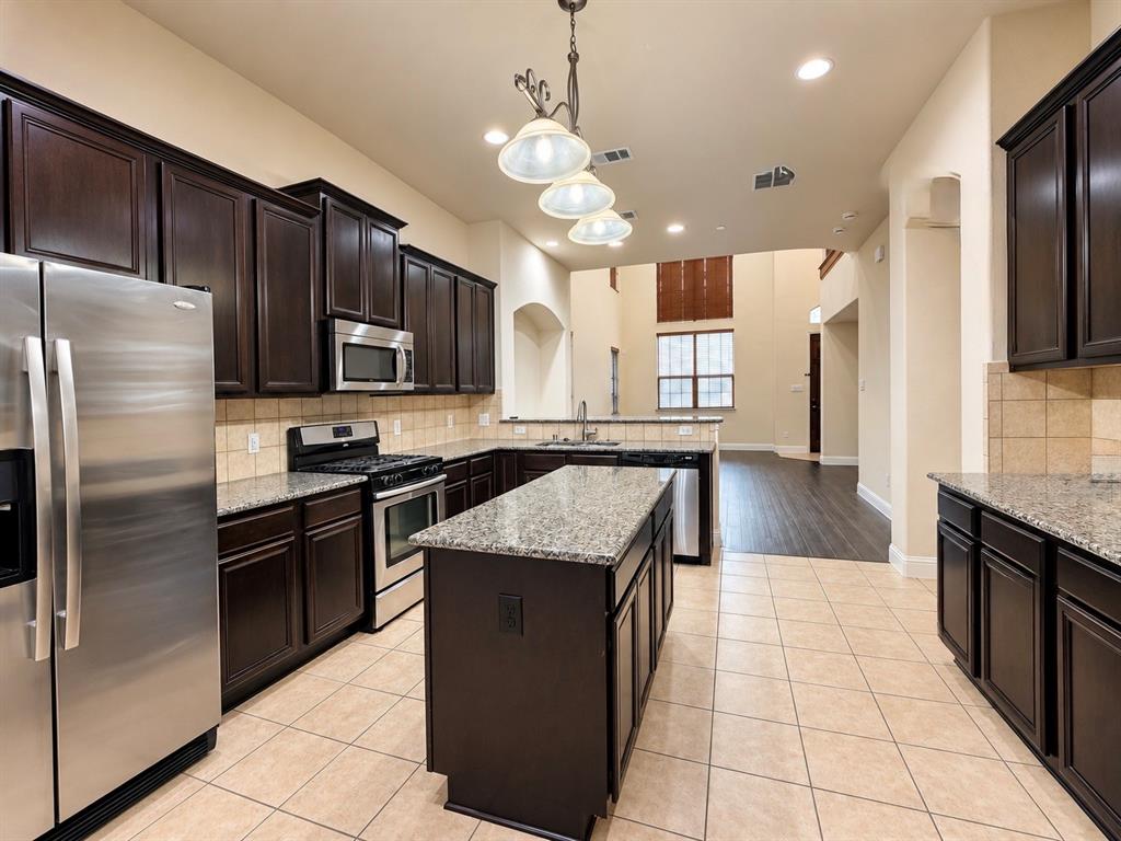 Kitchen featuring dark wood cabinetry, stone countertops, central island, stainless steel appliances, and tile flooring Kitchen featuring dark wood cabinetry, stone countertops, central island, stainless steel appliances, and tile flooring