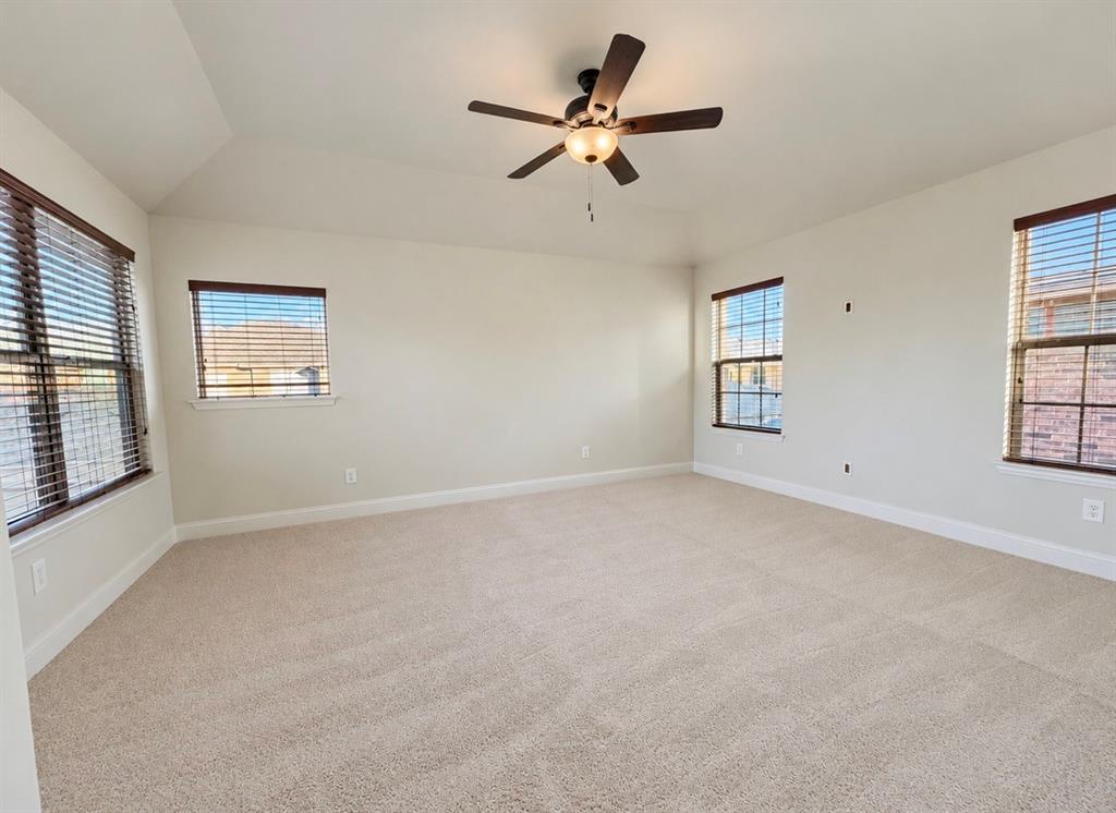 Neutral-toned room featuring a tray ceiling, wall-to-wall carpeting, multiple windows with blinds, and a central ceiling fan with an integrated light fixture