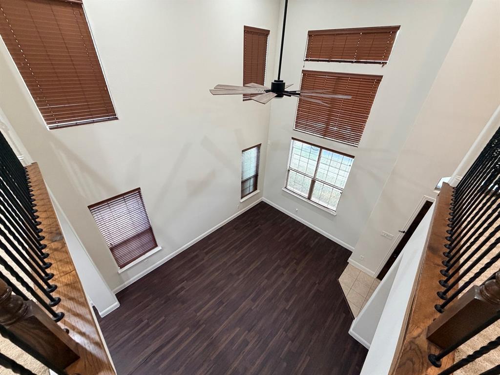 Double-height ceiling featuring wood-finish flooring, multiple oversized windows, wooden slat blinds, and a suspended ceiling fan
