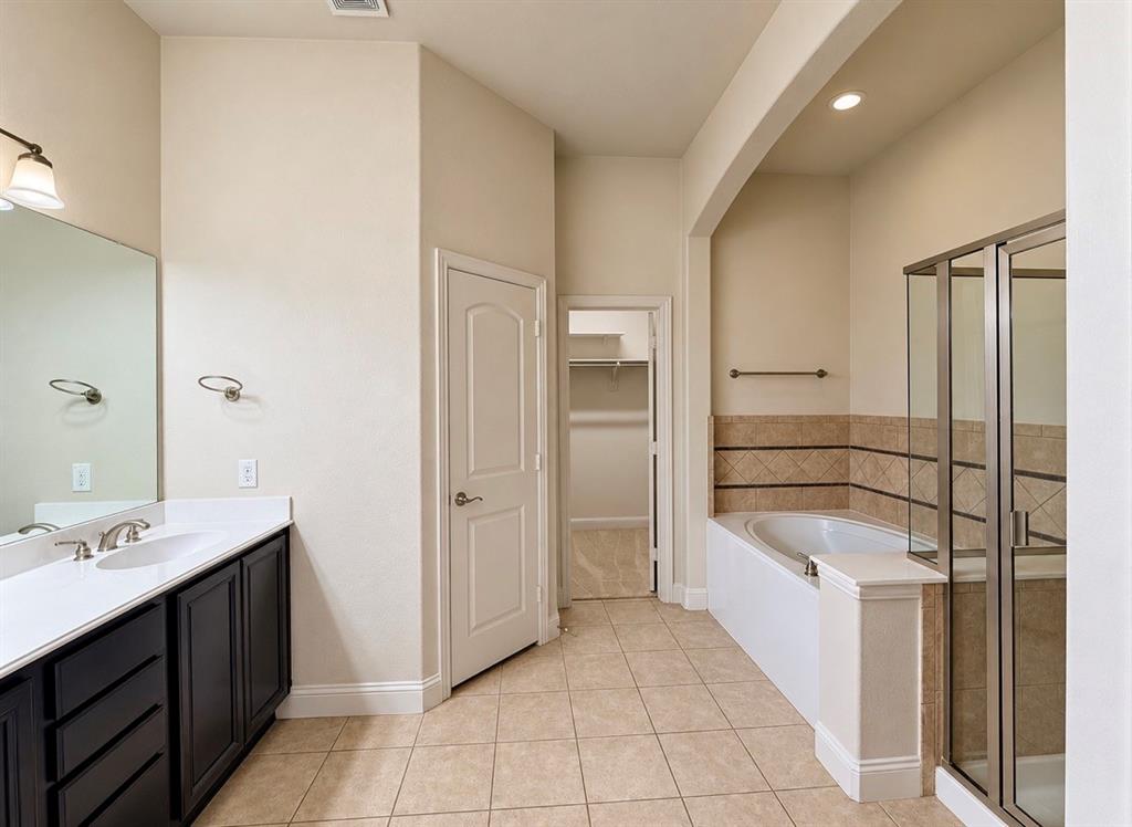 Bathroom featuring dark-finish cabinetry with a white countertop, undermount dual sinks, a jetted soaking tub with tile surround, and a glass-enclosed shower