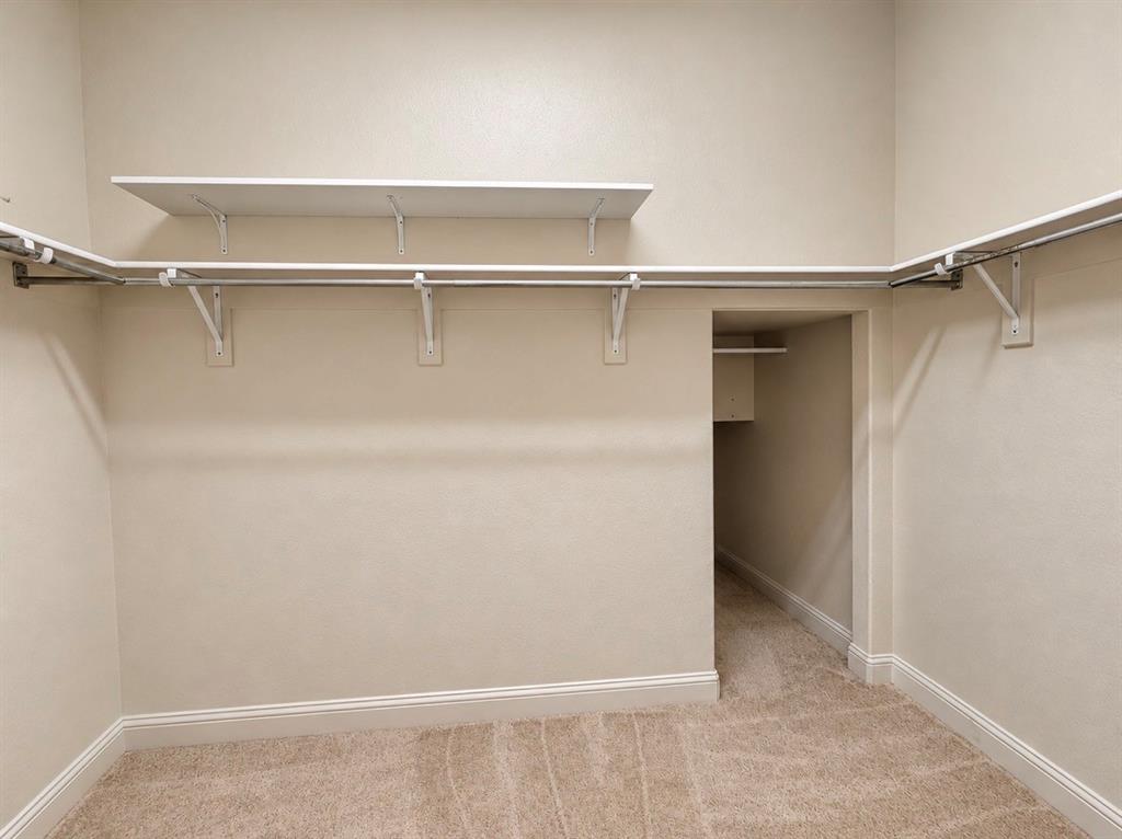 Walk-in closet featuring wall-to-wall carpeting, tiered shelving, metal hanging rods, and a supplemental storage nook
