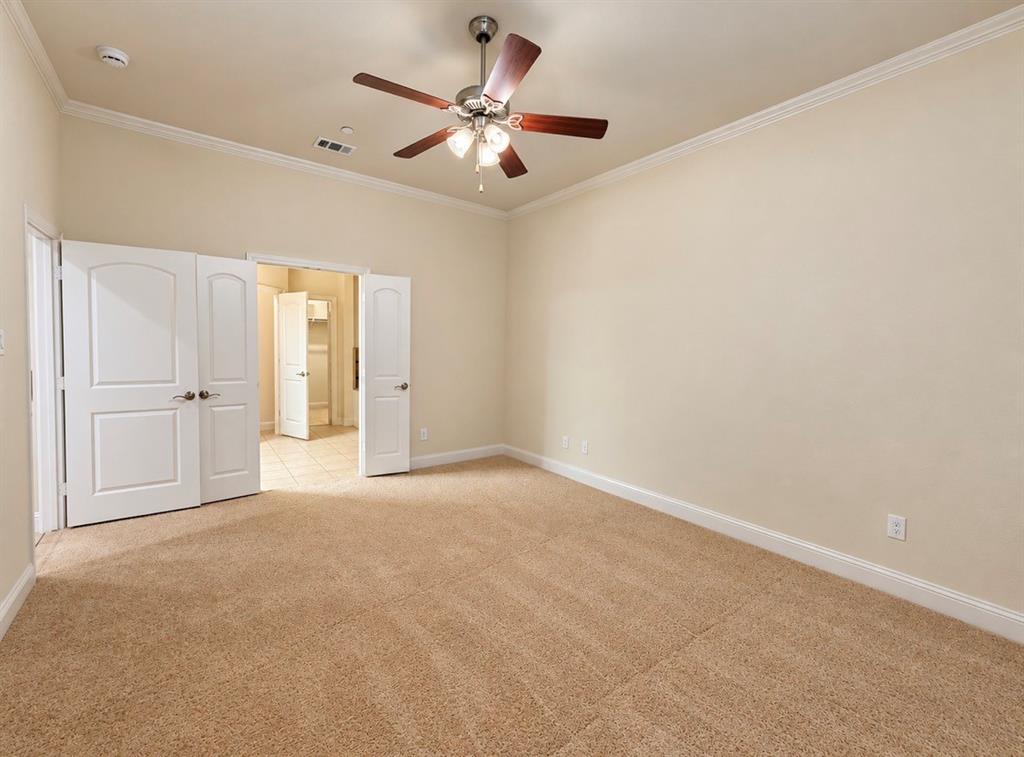 Room featuring neutral carpeting, crown molding, multi-panel arched doors, and a ceiling fan with integrated lighting