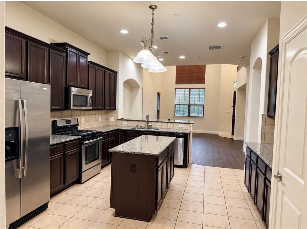 Kitchen featuring dark wood cabinetry, an expansive center island, stone-finish countertops, stainless steel appliances, and tile flooring