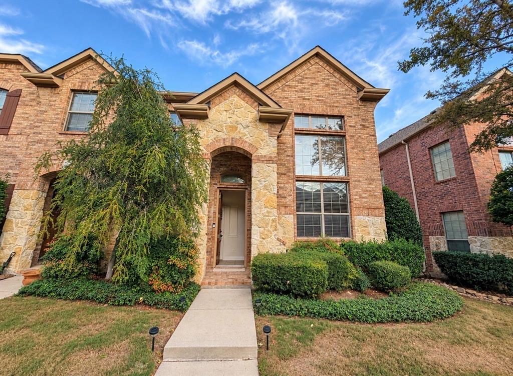 Two-story brick and stone facade featuring an arched entryway, multi-pane windows, and a concrete front walkway Two-story brick and stone facade featuring an arched entryway, multi-pane windows, and a concrete front walkway
