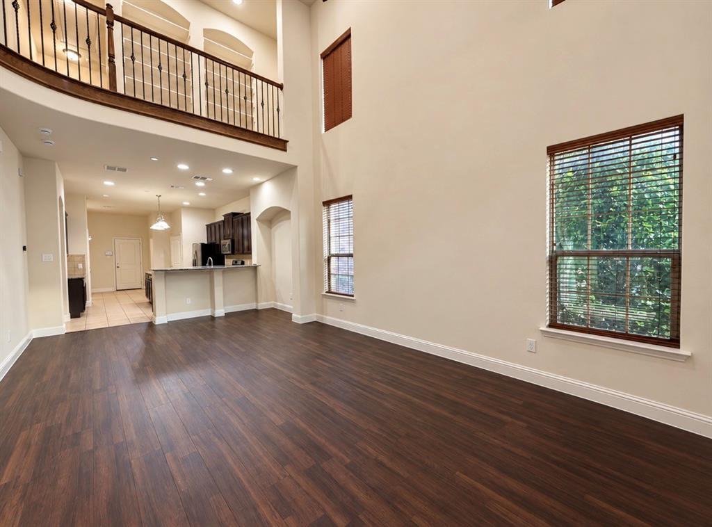 Double-height ceiling, wood-finish flooring, wrought iron staircase railing, recessed lighting, and built-in kitchen cabinetry with a breakfast bar