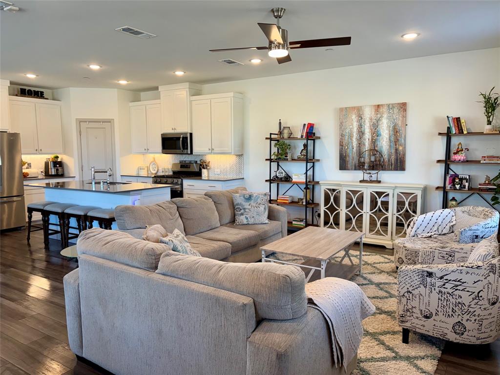 Open-concept kitchen featuring white shaker-style cabinetry, dark stone countertops, an oversized island, recessed lighting, and wood-finish flooring