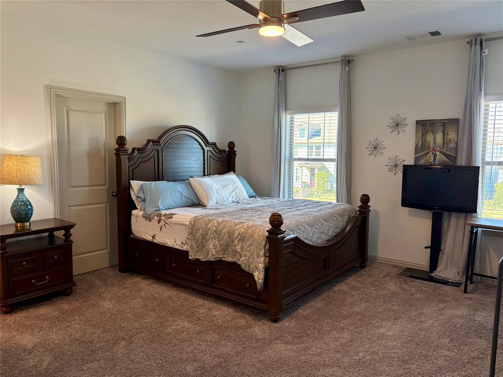 Spacious bedroom featuring wall-to-wall carpeting, dual windows, and an integrated ceiling fan with central light fixture