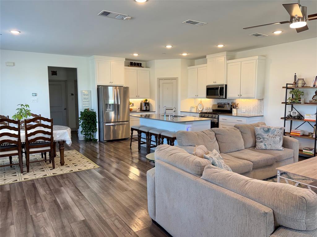 Open-concept interior featuring wood-finish flooring, white cabinetry, stainless steel appliances, a central kitchen island with countertop seating, and recessed lighting