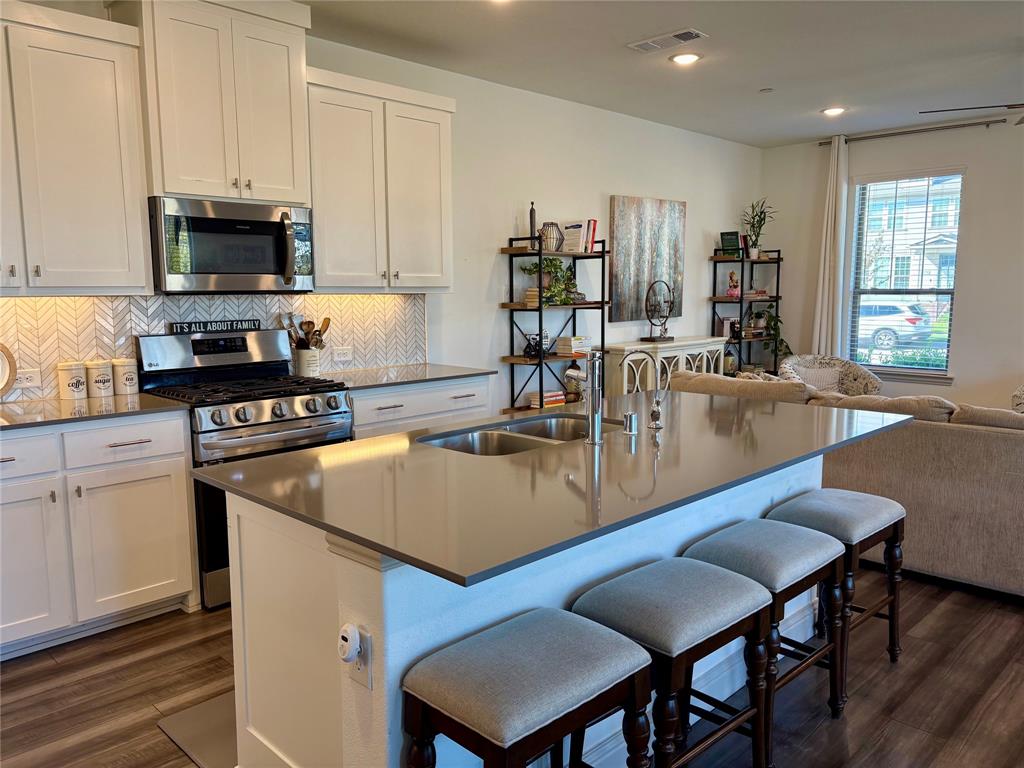 Kitchen featuring a large central island with a solid surface countertop, white shaker-style cabinetry, a herringbone-pattern tile backsplash, stainless steel appliances, and wood-finish flooring
