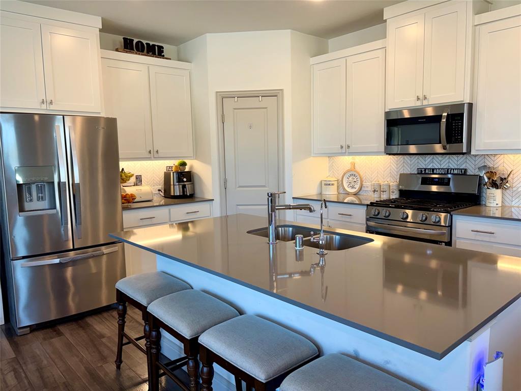 Kitchen featuring white shaker-style cabinetry, stainless steel appliances, a central island with a solid-surface countertop, and a herringbone-patterned tile backsplash