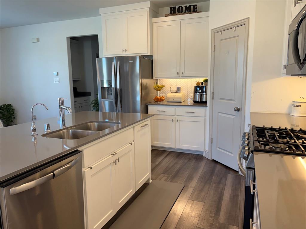 Kitchen featuring white shaker-style cabinetry, quartz countertops, stainless steel appliances, a central island with an undermount sink, and wood-finish flooring
