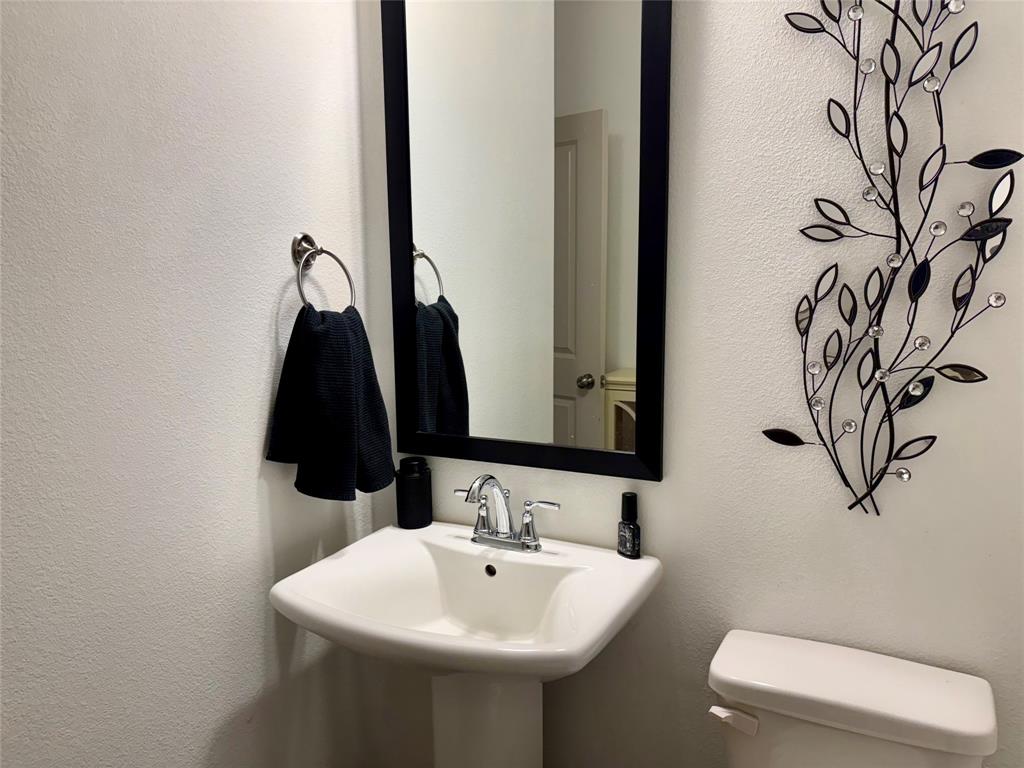 Pedestal sink featuring a polished chrome dual-handle faucet, wall-mounted circular towel ring, and rectangular mirror with a black frame