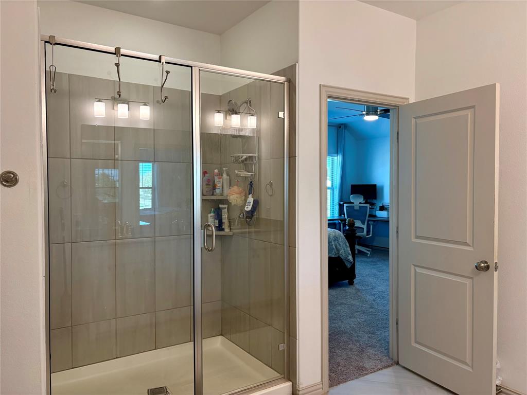 Walk-in shower with floor-to-ceiling ceramic tile surround, glass enclosure, chrome hardware, and a built-in corner shelving unit