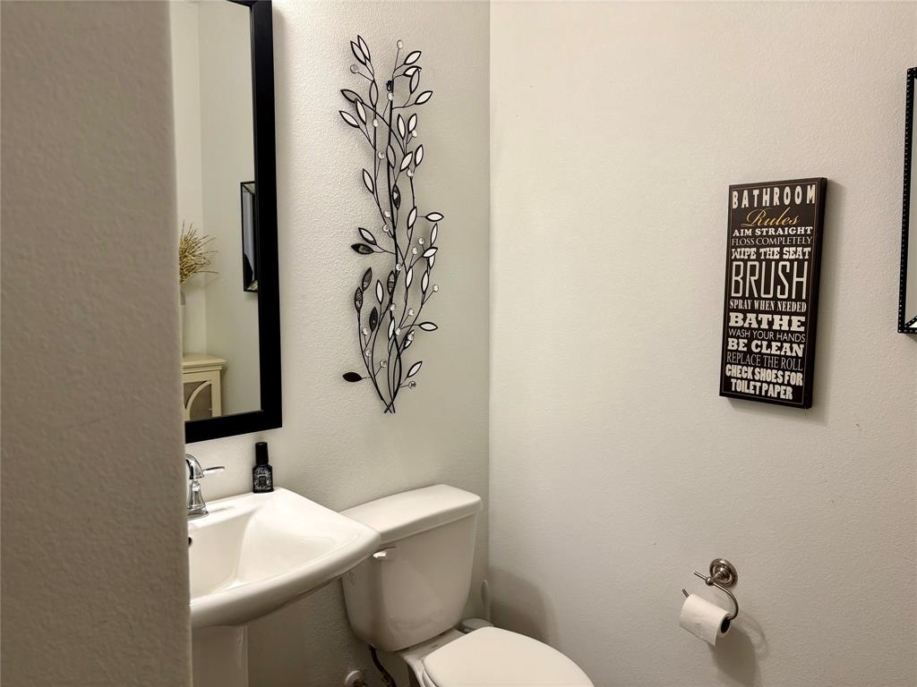 Wall-mounted rectangular mirror with a black frame, pedestal sink with a chrome finish faucet, and polished chrome toilet paper holder