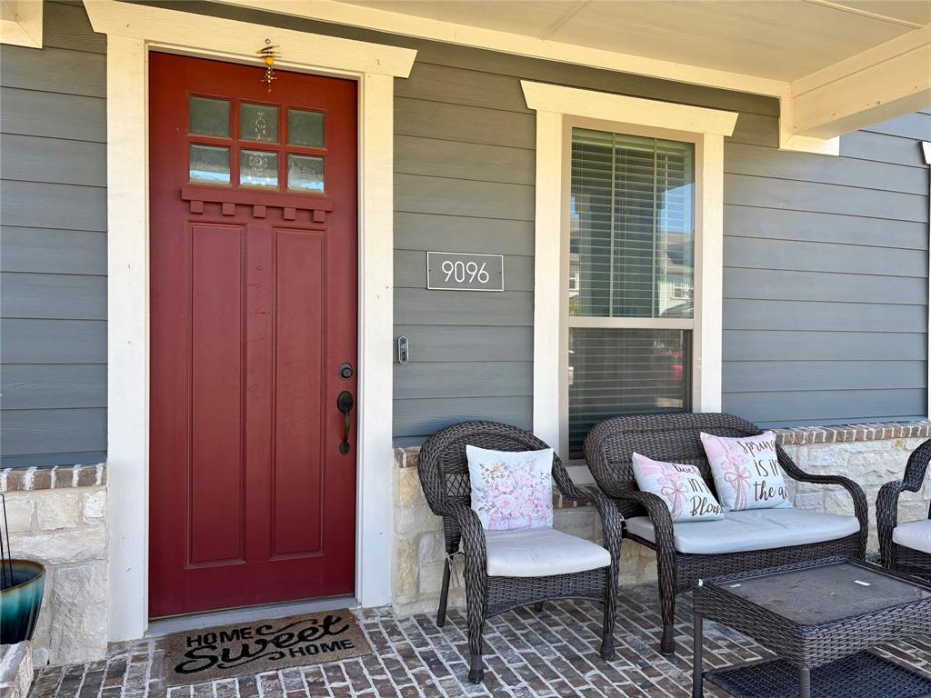 Covered porch featuring horizontal lap siding, stone veneer accents, a red paneled entry door with a multi-pane glass inlay, and brick-patterned flooring