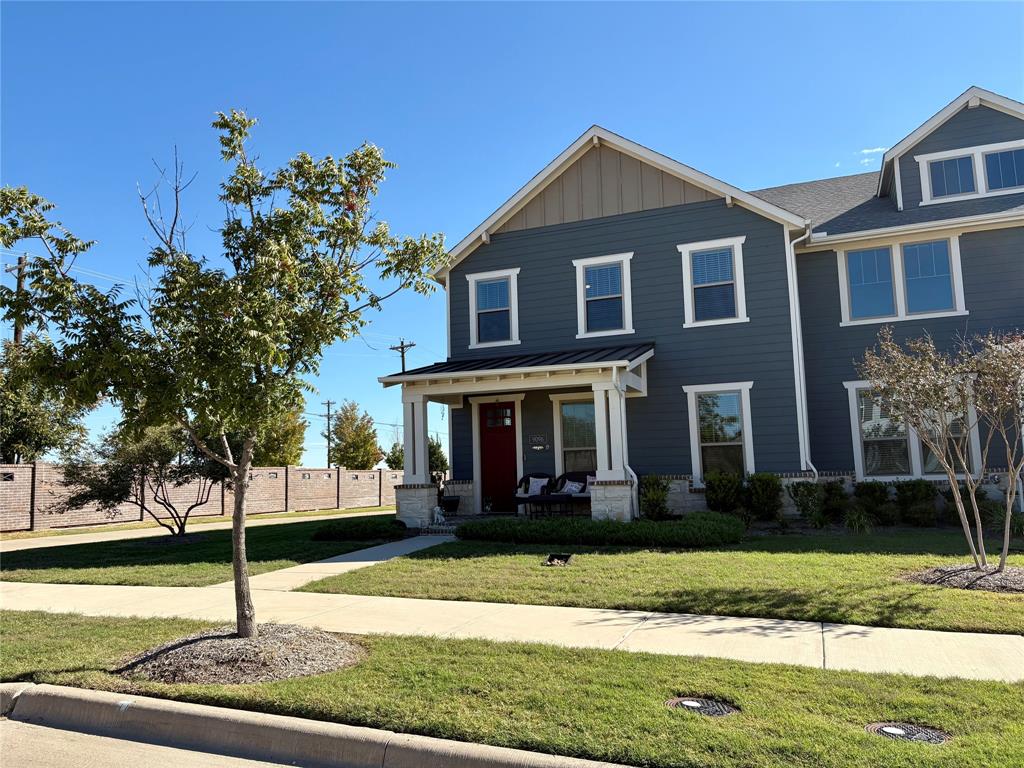 Two-story residence featuring blue horizontal lap siding, stone veneer accents, a covered front porch with tapered columns, a metal roof accent, and a solid-color entry door