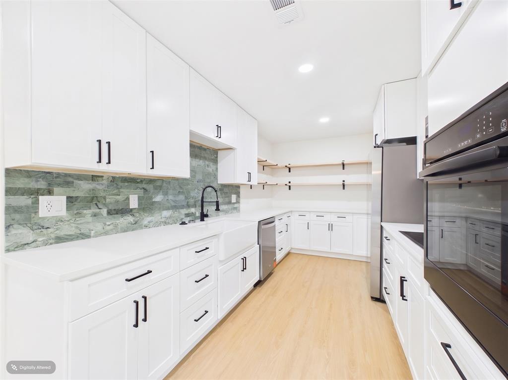 Kitchen featuring white shaker cabinetry, stone tile backsplash, farmhouse-style sink, matte black hardware, and light-toned wood-finish flooring