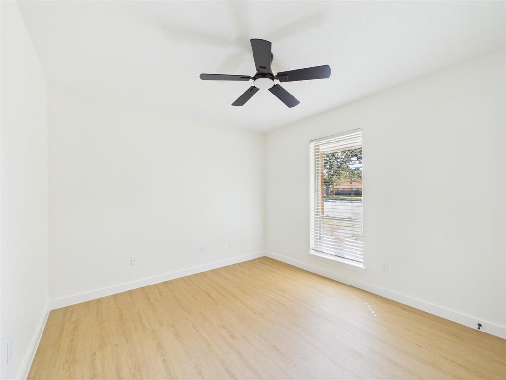 Neutral-toned interior featuring wood-finish flooring, a matte black five-blade ceiling fan with integrated lighting, and a vertical window equipped with horizontal blinds