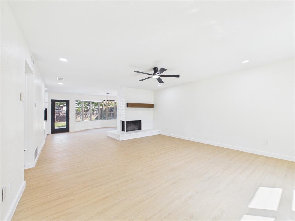 Open interior featuring light wood-finish flooring, white brick fireplace with a wood mantle, recessed lighting, and a ceiling fan
