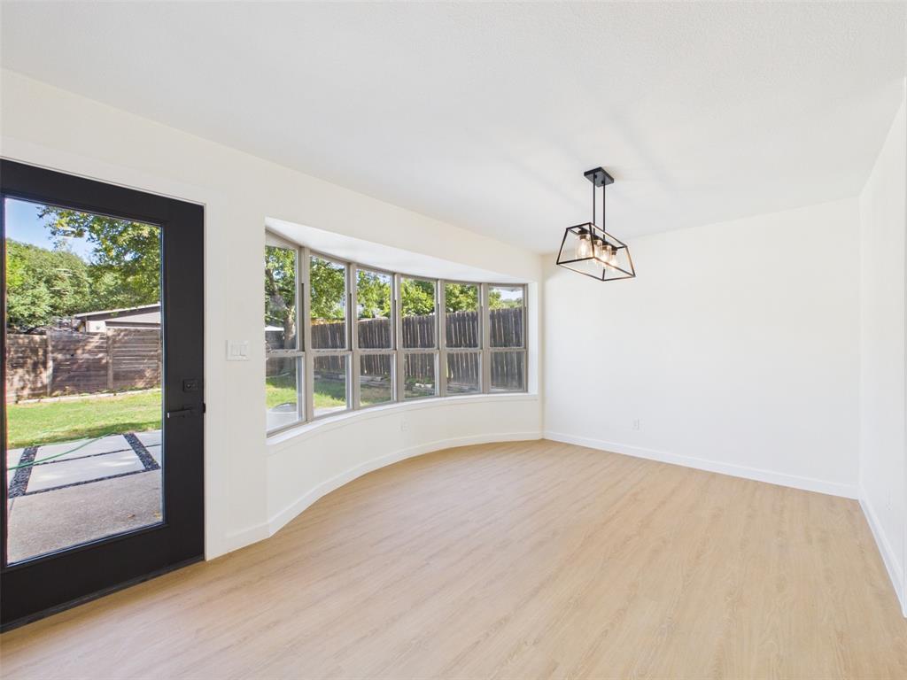 Curved bay window with large-pane windows, wood-finish flooring, matte black framed glass door, and geometric four-light pendant fixture