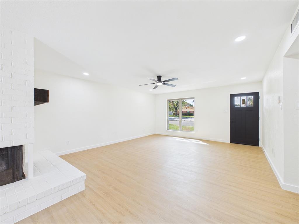 Open living area featuring wood-finish flooring, a white painted brick fireplace, recessed lighting, a matte black ceiling fan, and a black paneled exterior door with glass detailing