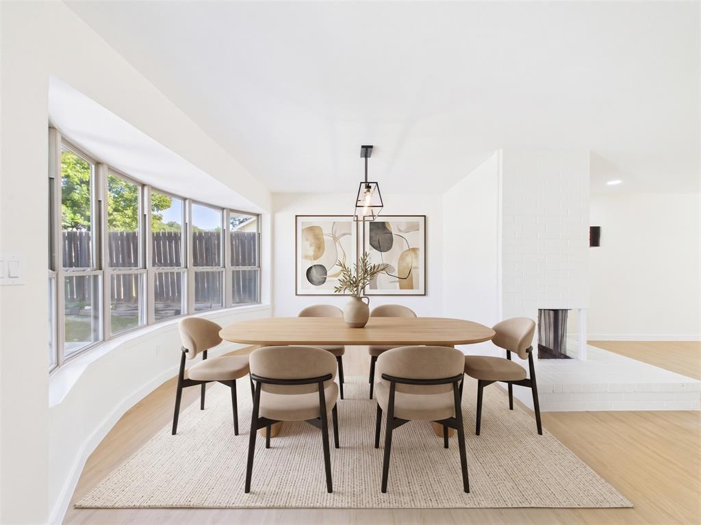 Expansive bay window, wood-finish flooring, white-painted brick fireplace, and geometric pendant lighting