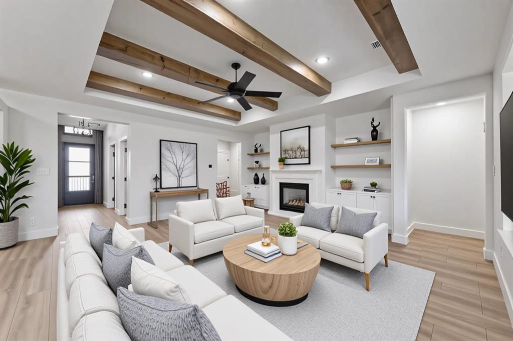 Living room with a tray ceiling, a glass covered fireplace, light wood finished floors, and a ceiling fan