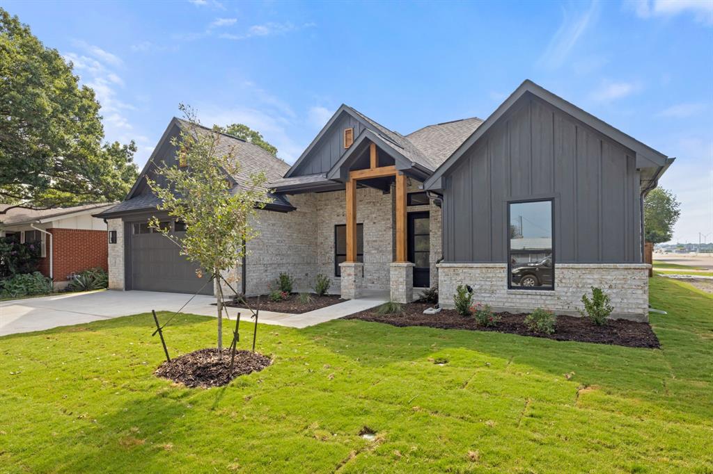 View of front facade with stone siding, an attached garage, a front lawn, board and batten siding, and driveway