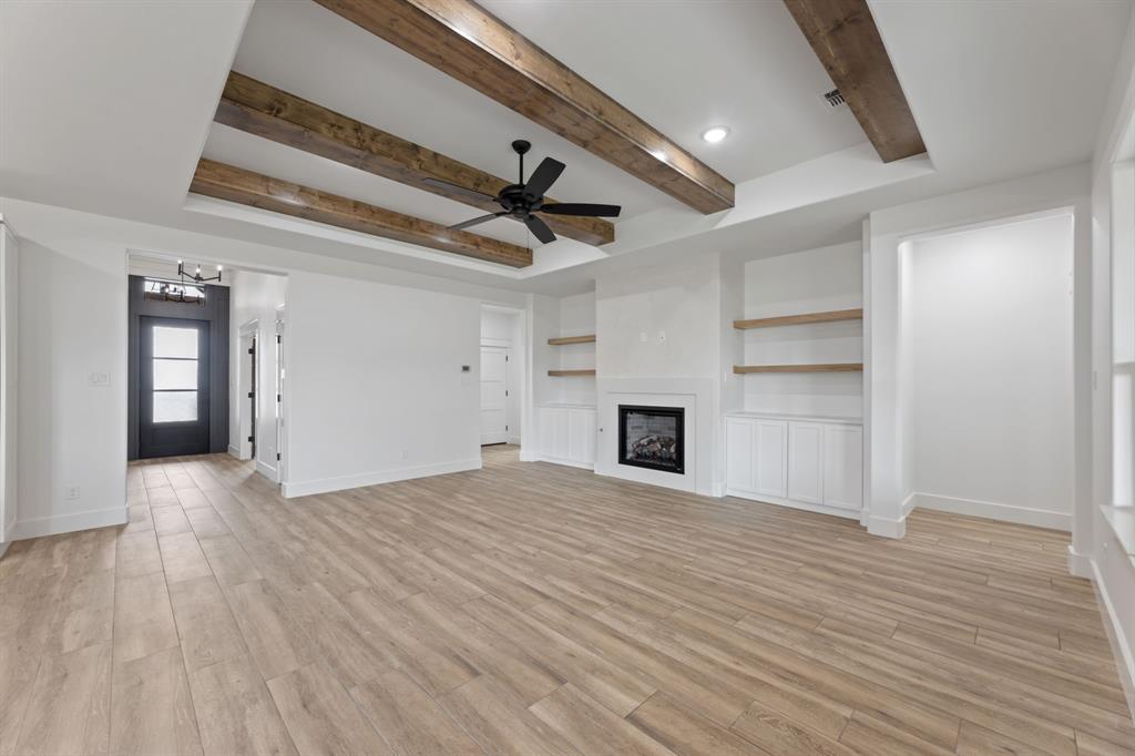 Unfurnished living room featuring beam ceiling, ceiling fan with notable chandelier, baseboards, and light tile finished floors